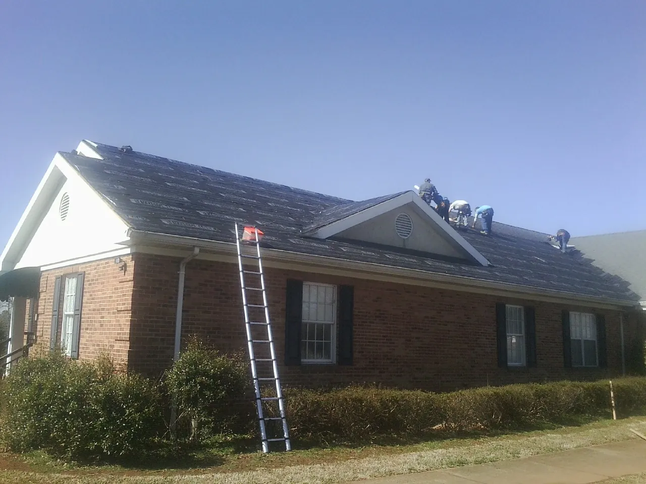 Crew tearing shingles off a brick ranch roof with a ladder set — Metal Roof Repair work by our crew in Maugansville