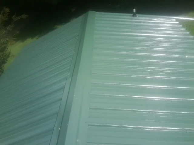 New green metal panels meeting at the ridge of a roof — Flat Roof Repair work by our crew in Maugansville