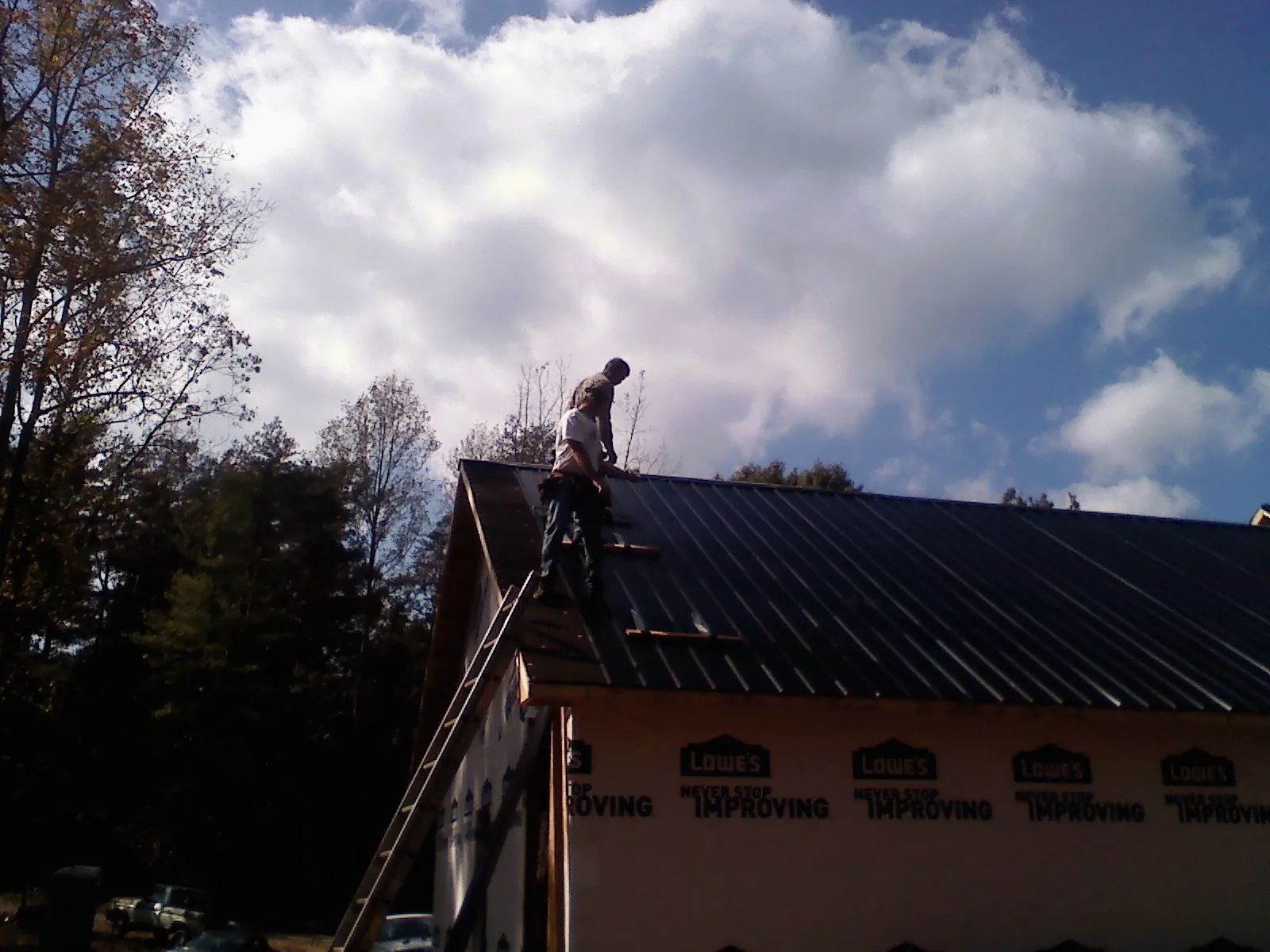 Roofer fastening dark metal panels high against a cloudy sky, from a Roof Inspection job in Maugansville