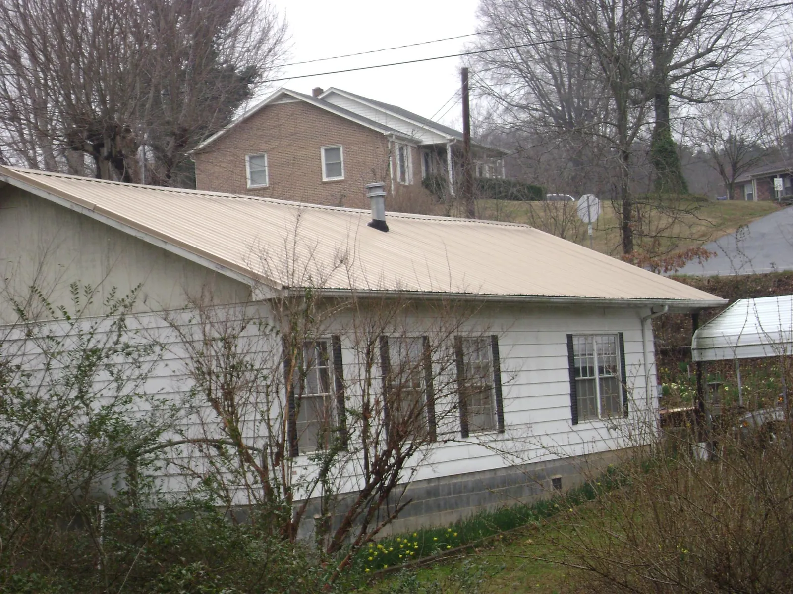 Tan metal roof on a white sided house set into a hillside — Commercial Roofing by Roofing Brothers in Maugansville
